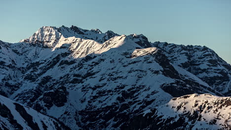 Toma-En-ángulo-Bajo-Del-Hermoso-Pico-De-La-Montaña-De-Invierno-Blanco-Cubierto-De-Nieve-En-El-Tiempo-De-La-Tarde-Con-El-Sol-Bajando-A-Lo-Largo-Del-Costado-En-El-Lapso-De-Tiempo