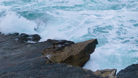 sea waves breaking on rocky shore creating foam and mist on stormy weather - close up