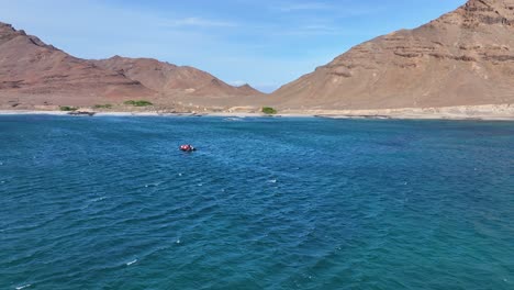 Aerial-View-of-Boat-Sailing-in-Front-of-Santa-Luzia,-Uninhabited-Volcanic-Island-in-Cape-Verde-Archipelago,-Drone-Shot