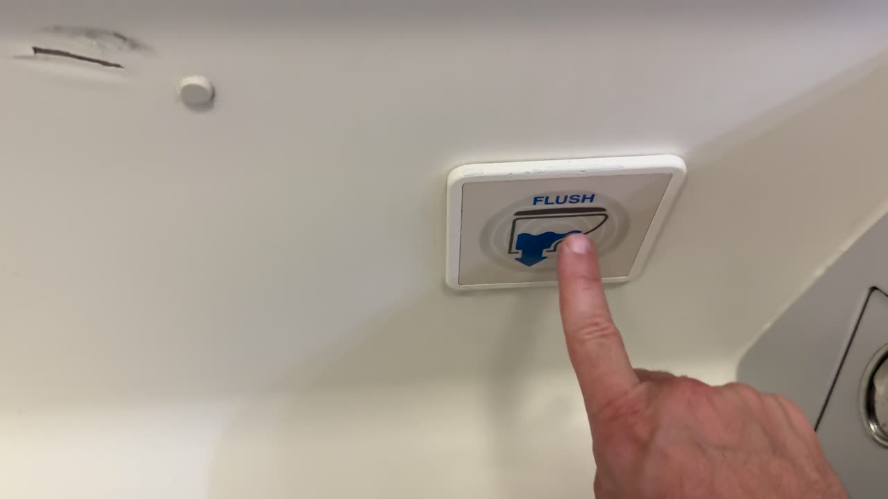Hand presses flush button in airplane lavatory, bright lighting, static camera, close-up perspective