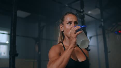 a tired female athlete in the gym drinks water from a bottle after training