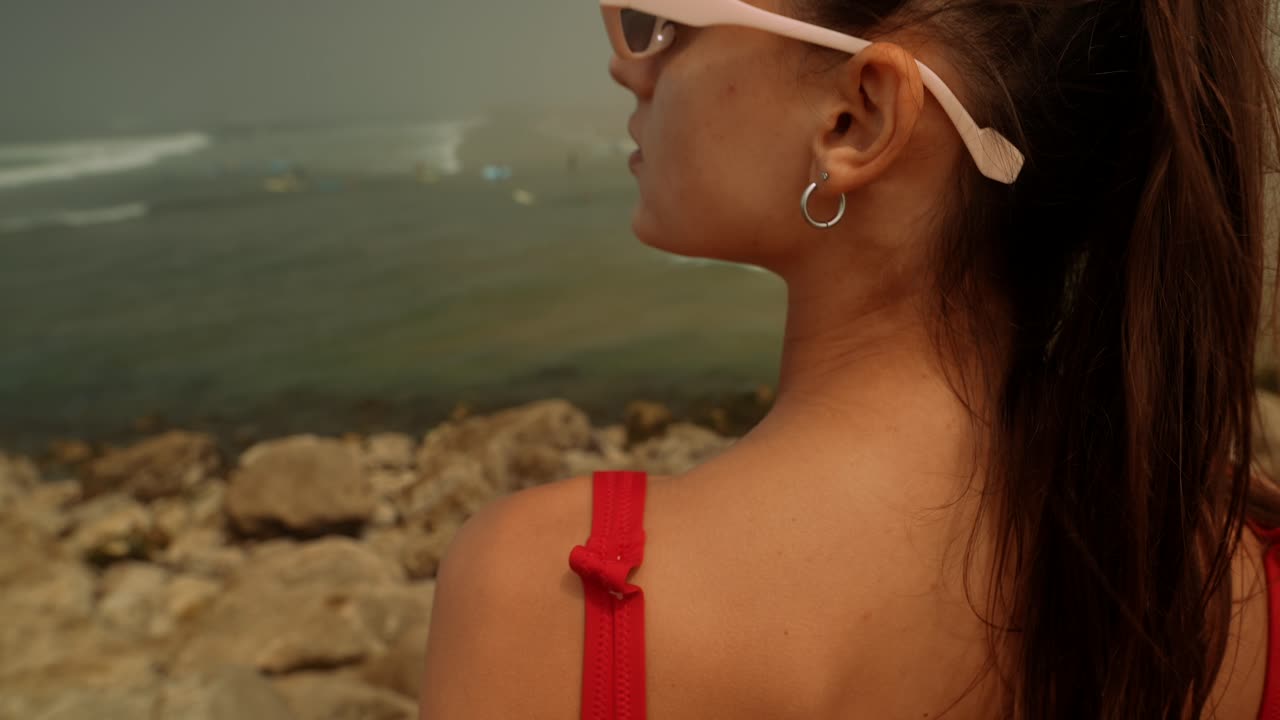 Giovane donna in costume da bagno rosso che guarda le onde dell'oceano