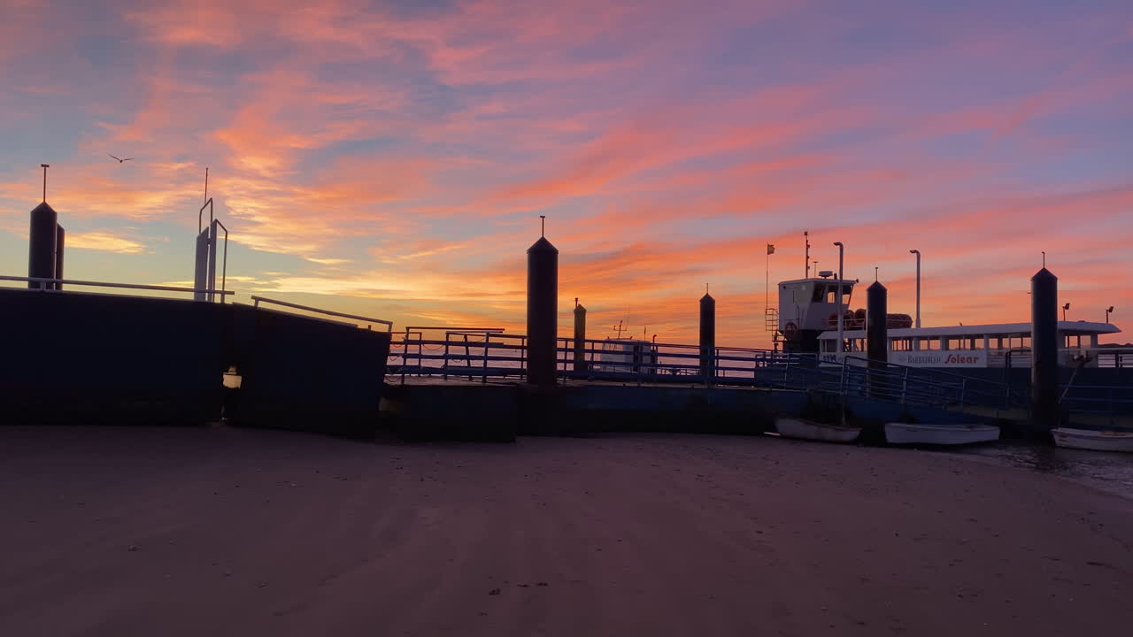 Doñana-färjan vilar vid lågvatten på Sanlucar de Barramedas strand medan flammande moln målar himlen i livfulla solnedgångsfärger