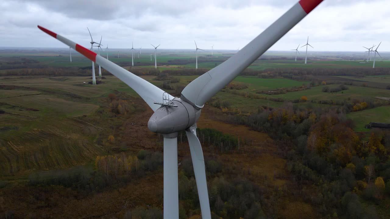 Aerial shot of multiple spinning wind turbines for renewable electric power production in a wide rural area on a cloudy day