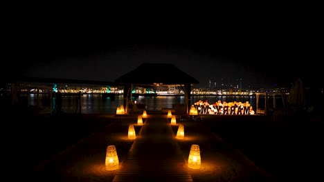 experience a romantic night dinner by the shore for a couple, with candles illuminating the pathway