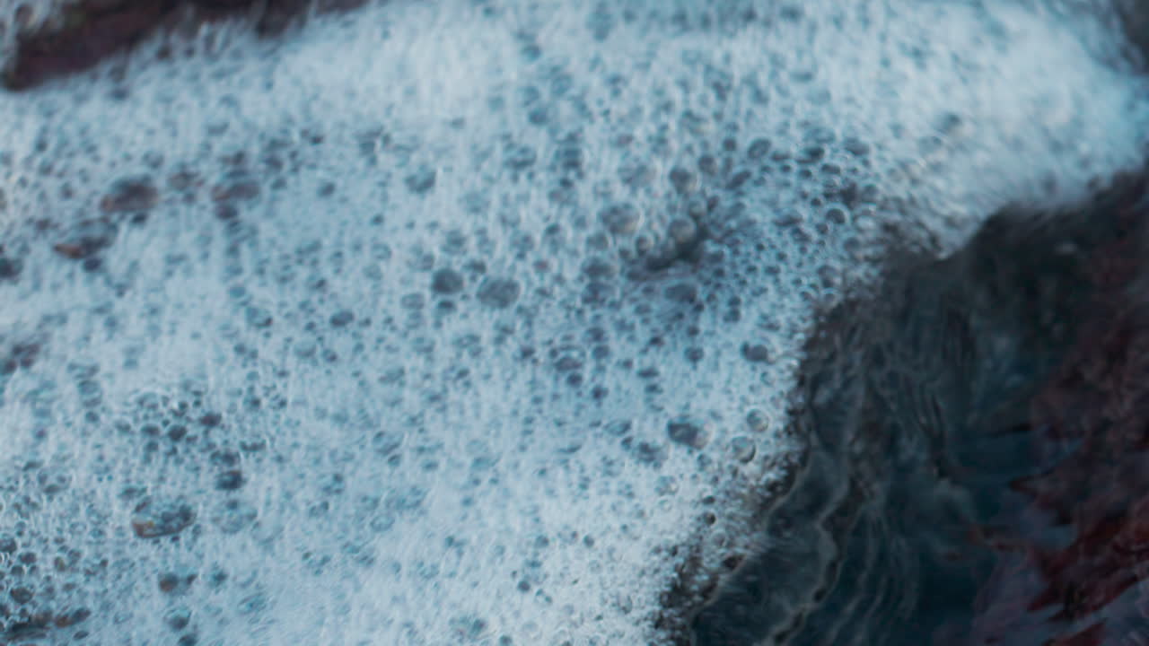 Close up of seawater swirling between coastal rocks, forming white foam and bubbles