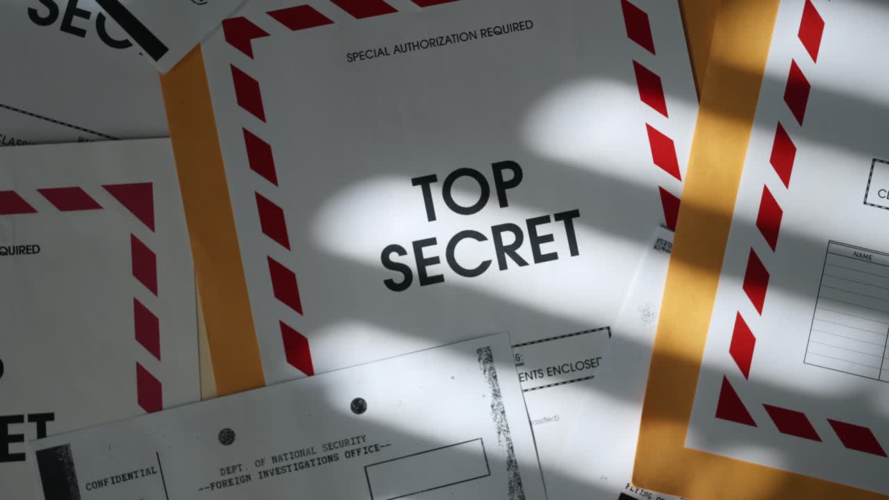 Close up on Top Secret label on manila envelope with classified documents. Dark office room and desk with window shadow on stack of papers with sensitive information and censored text