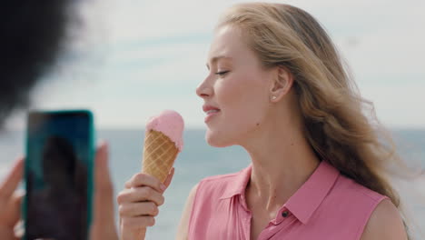 beautiful blonde woman with afro eating ice cream on beach posing for friend taking photo using smartphone girl friends sharing fun summer day on social media 4k