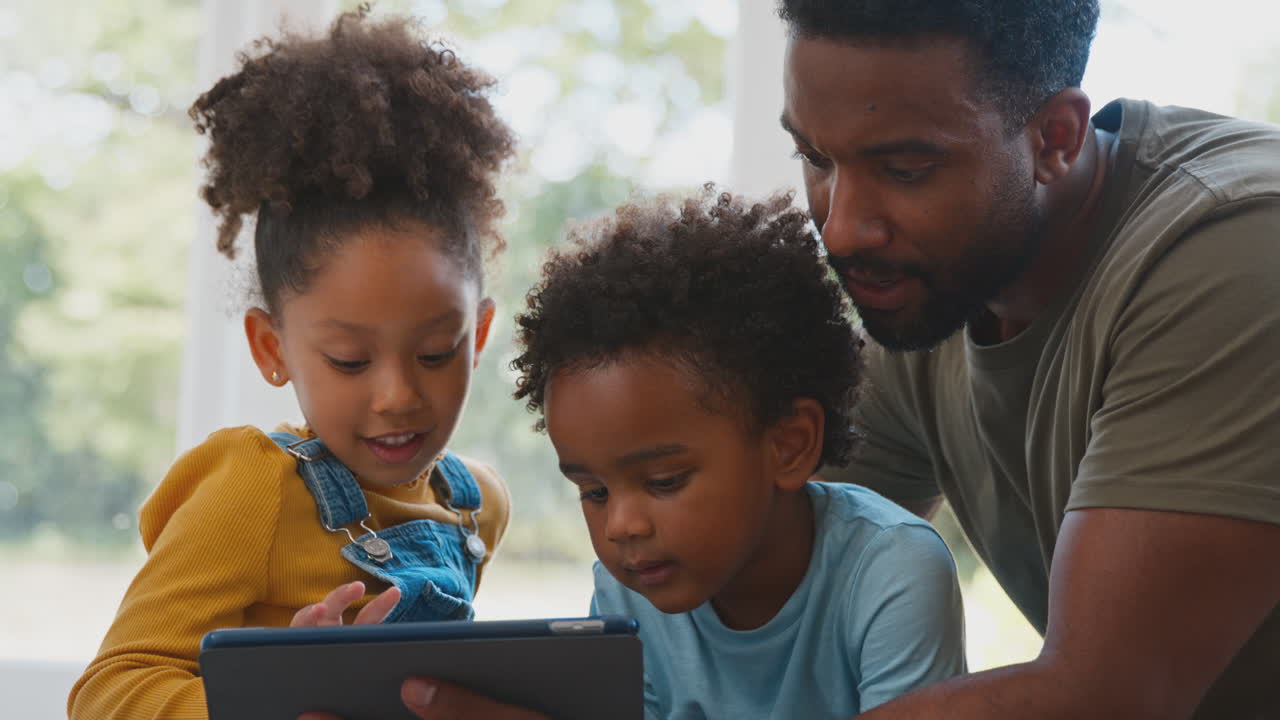 Padre a casa con i figli seduti sul tappeto che giocano con un tablet digitale