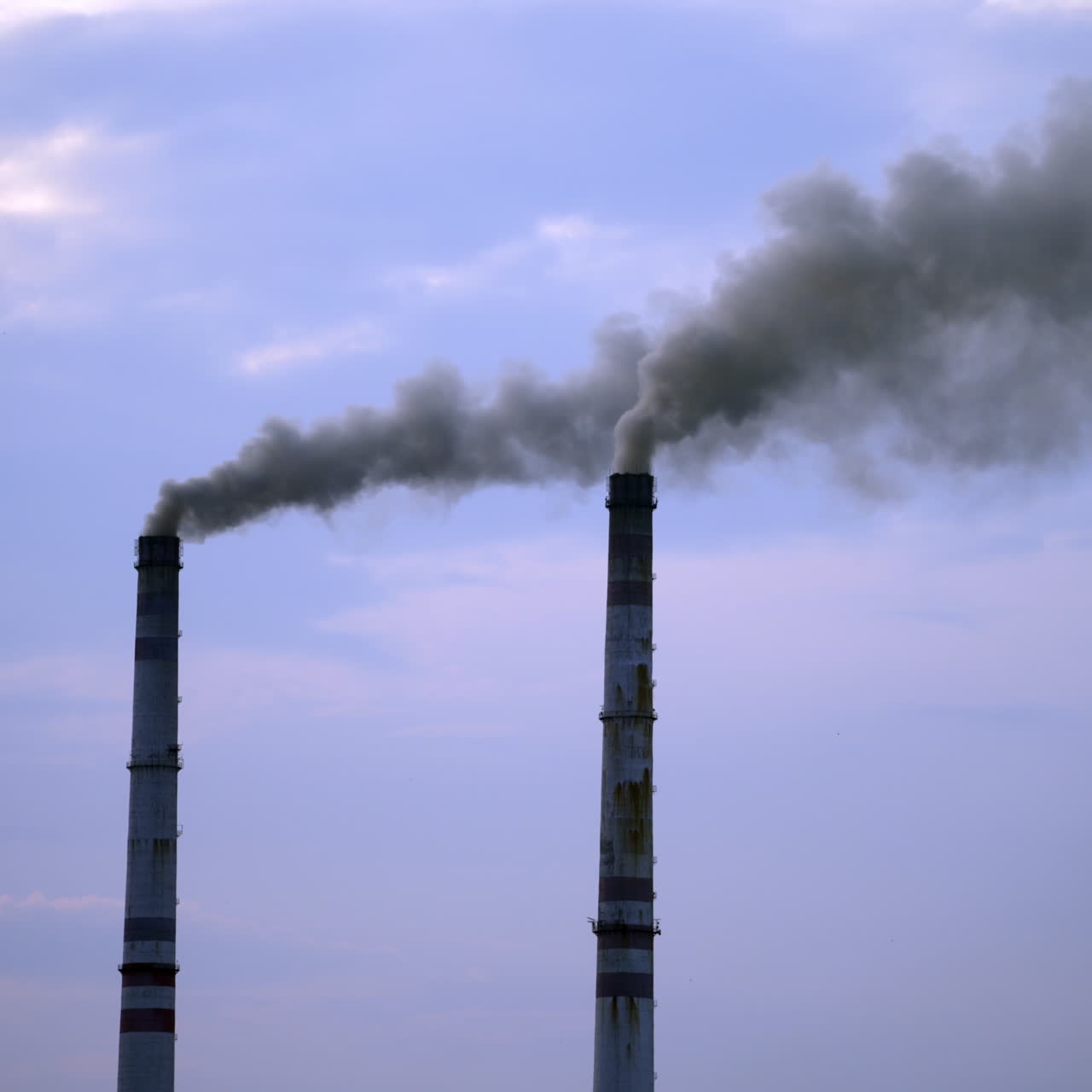 Industrial pipes pollute the atmosphere with smoke. Two big pipes with thick smoke in the air on the blue sky background.