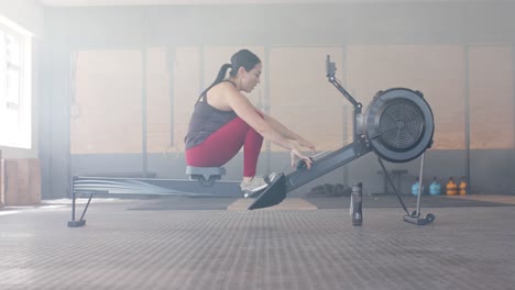 Mujer-Birracial-Determinada-E-Inalterada-Haciendo-Ejercicio-En-La-Máquina-De-Remo-En-El-Gimnasio,-En-Cámara-Lenta