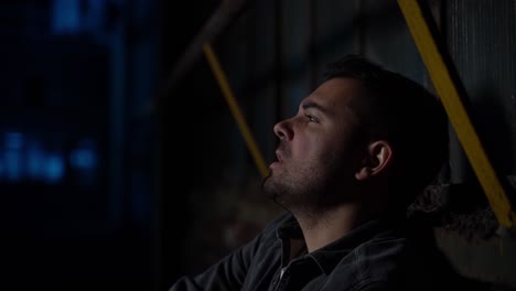 man sitting on the ground leaning to a wall in an dark abandoned industral place singing and sceaming sadly and angry