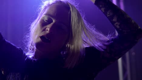 Slow-motion-handheld-shot-of-a-dancing-blonde-singer-during-a-live-performance-with-light-show-in-purple-light-in-a-concert-hall