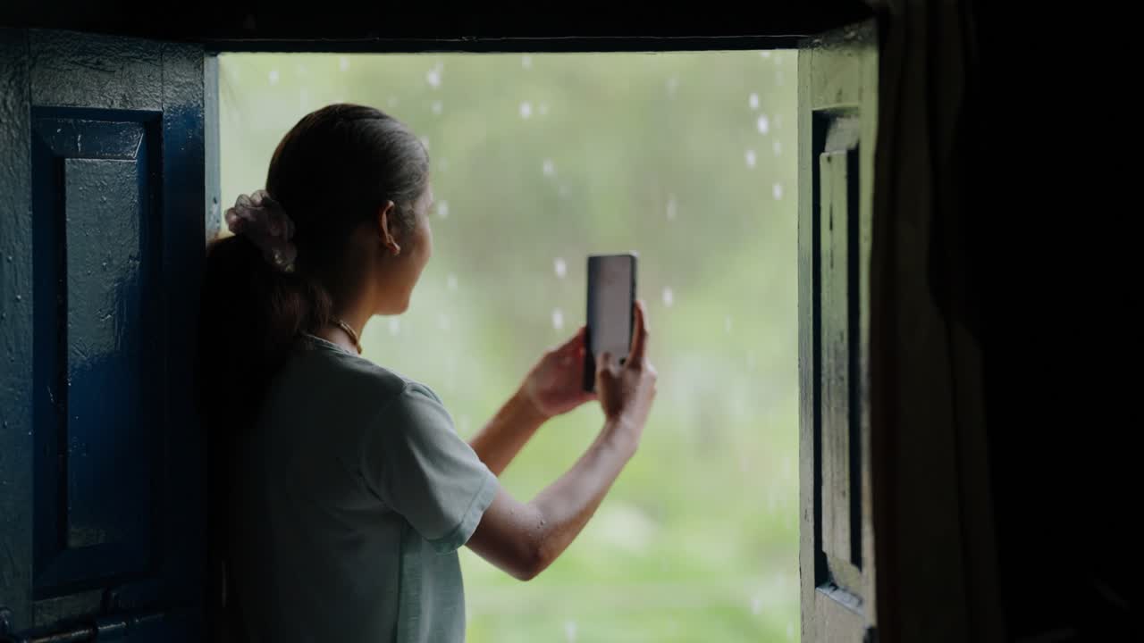 Calm and happy Indian girl watching rainfall from doorstep, authentic rural moment, 4k video