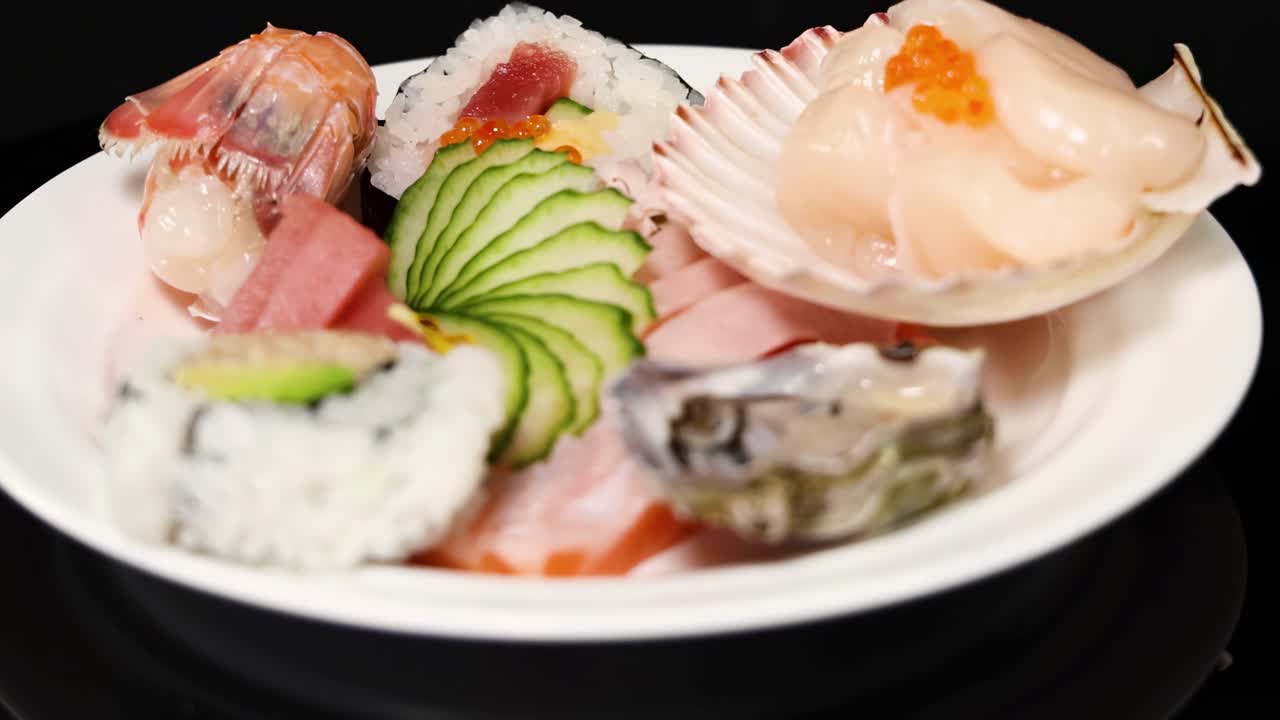 A close-up view of a sushi plate featuring shellfish, nigiri, and cucumber slices on a black background.