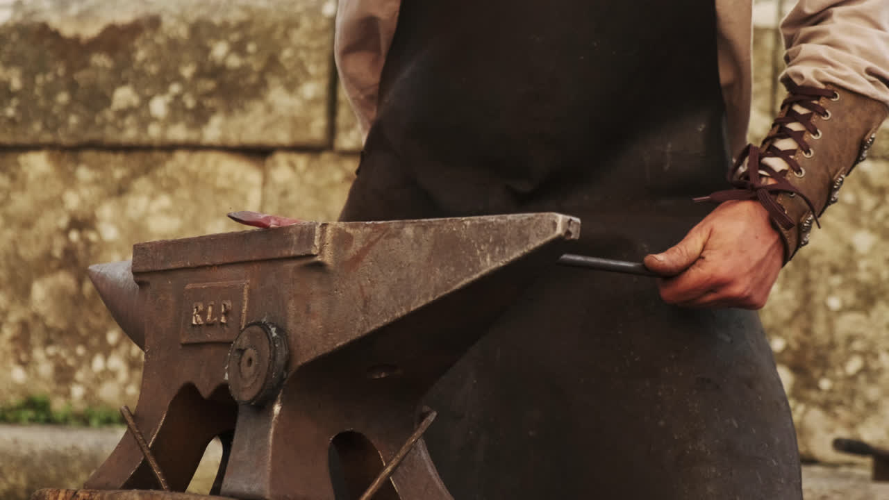 Slight low-angle static shot of a blacksmith hammering red-hot iron on an anvil; bright sparks fly with each blow, gritty workshop atmosphere in natural daylight
