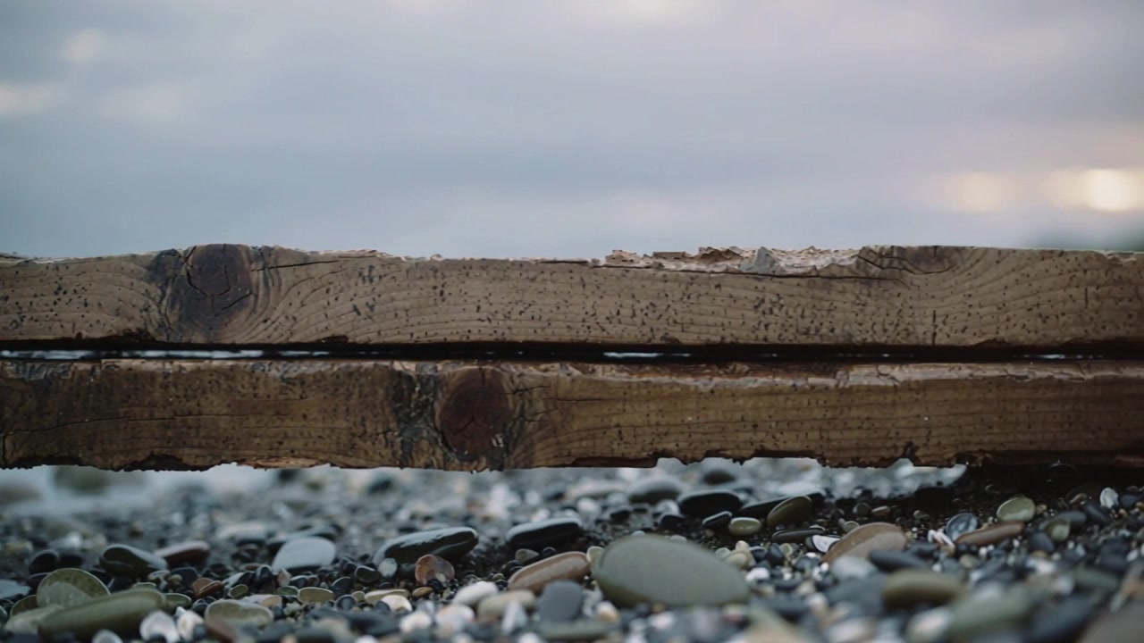 Una lente ad angolo basso rifocalizza, mettendo a fuoco assi consumate e ciottoli in spiaggia, mostrando un bagliore.
