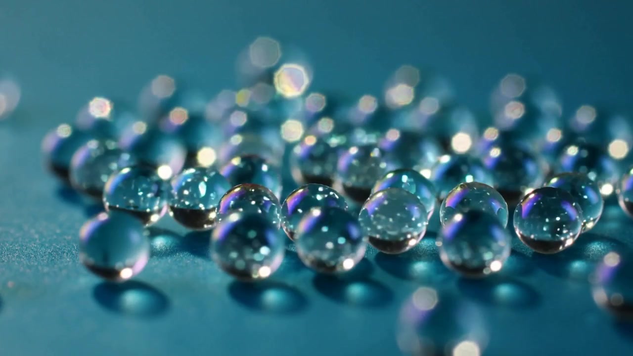Messa a fuoco della fotocamera che si sposta, un gruppo di perline trasparenti che mostrano riflessi interni su un tavolo color verde acqua, con bagliore bokeh.