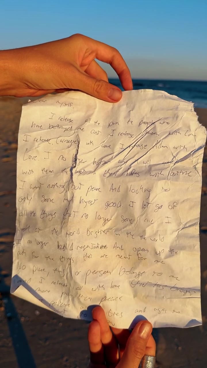 Mano che tiene un messaggio in una bottiglia. Mani che tengono una nota scritta a mano sulla spiaggia, simboleggiando il rilascio emotivo, il perdono e la riflessione personale in riva all'oceano