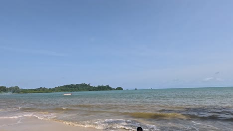 a smooth daytime camera pan reveals a quiet sandy beach, turquoise sea, and lush trees under clear blue skies on ko phayam island