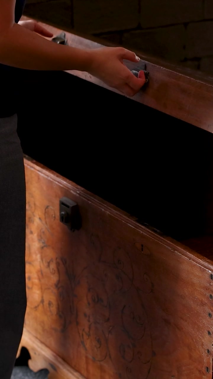 Primo piano di una persona che solleva il coperchio di un'antica cassa di legno all'interno.
