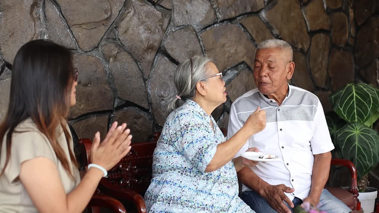 Happy Elderly Asian Mother Feeding Her Husband And Daughter With Birthday Cake Then Give Them Kiss On The Cheek