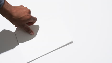 Video-of-hand-of-african-american-man-holding-book-with-blank-pages,-copy-space-on-white-background