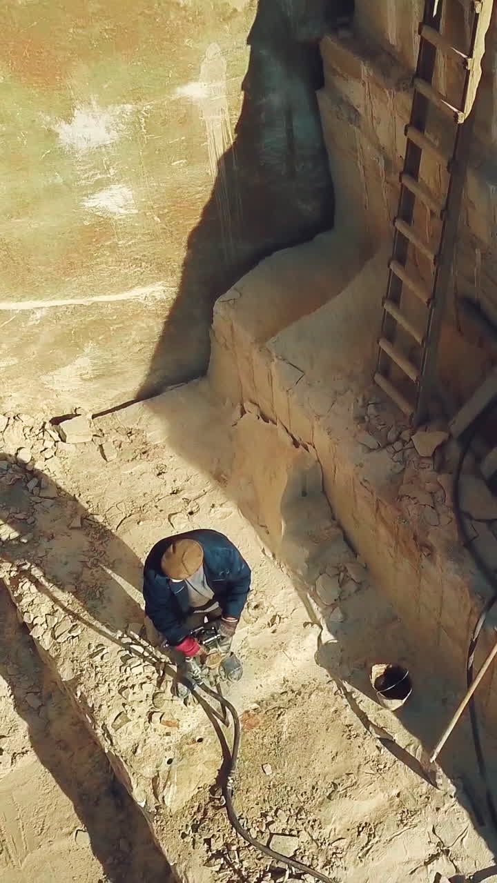 a man is drilling stones with using power tool in a sand quarry. Camera motion up Vertical video