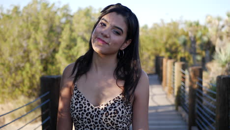 Cute-hispanic-woman-walking-in-slow-motion-along-a-wooden-bridge-outdoors-in-sunlight-smiling-and-looking-happy