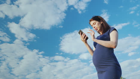 Eine-Schwangere-Frau-Benutzt-Ein-Smartphone-Gegen-Einen-Blauen-Himmel-Unterer-Blickwinkel