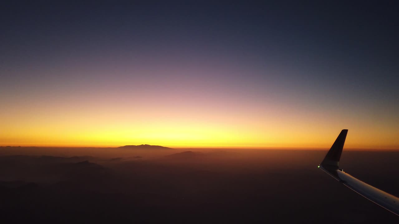 vista de ala de avión y silueta de montaña con horizonte amarillo y azul al amanecer, vista desde la ventana del avión