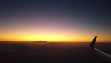 aircraft wing and mountain silhouette view with yellow and blue horizon in sunrise time, viewed from airplane window