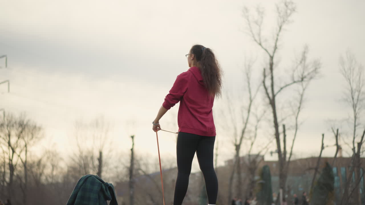 Person In Red Jacket Performs Resistance Stretch, Individual Engaging In Exercise With City Skyline Backdrop, Woman In Vibrant Attire Exercises With Resistance Band Against Urban Skyline Scenery