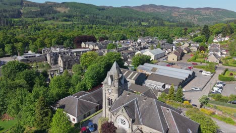 Drone ascending to reveal Pitlochry village behind the historic church, showcasing scenic highlands, charming streets, and surrounding green landscapes