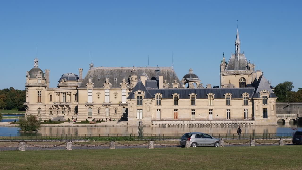 Front view of the Chateau de Chantilly castle with cars moving in front, in Chantilly, Oise, France in daylight