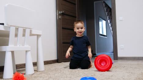 smiling baby sitting on the floor plays with pyramid. lovely baby boy rolling the toy ring by the carpet.