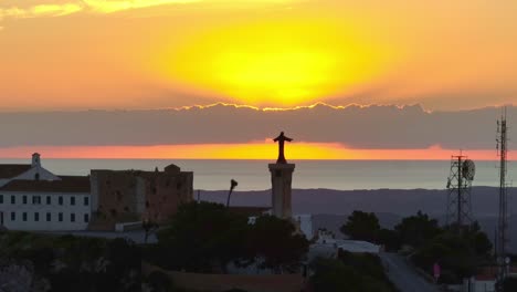 sunrise silhouettes with outline of jesus statue on spanish island in europe