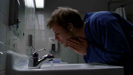 man washing face in bathroom sink