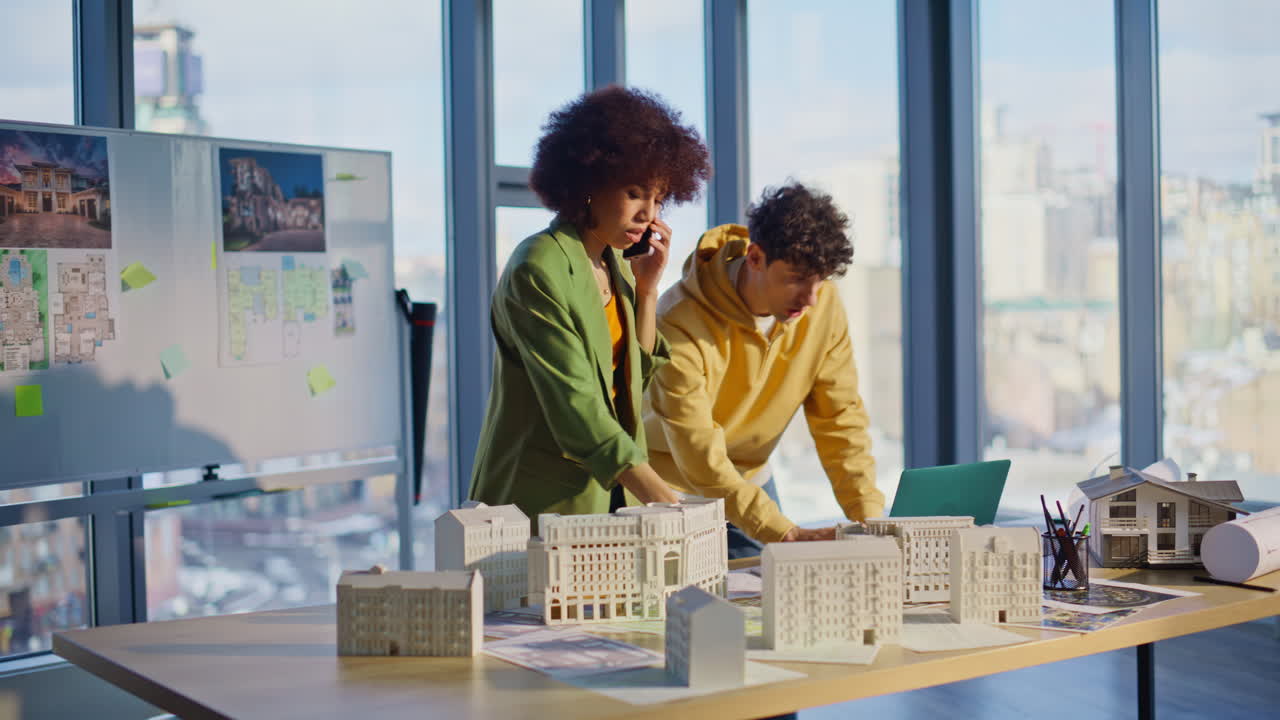 Nervous engineers talking mobile phone discussing architectural plan in office
