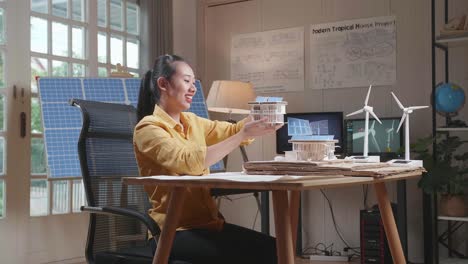 side view of asian woman positively shaking her head while holding and looking at model of small house with solar panel