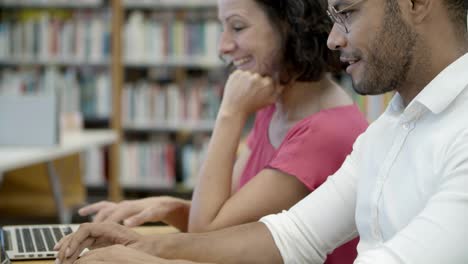 smiling people talking while using laptops at library