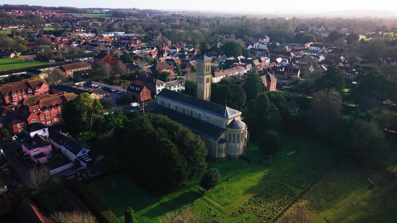 Riprese aeree con drone di una grande chiesa parrocchiale in pietra con un alto campanile in stile italiano, circondata dai tetti del villaggio e dagli alberi.
