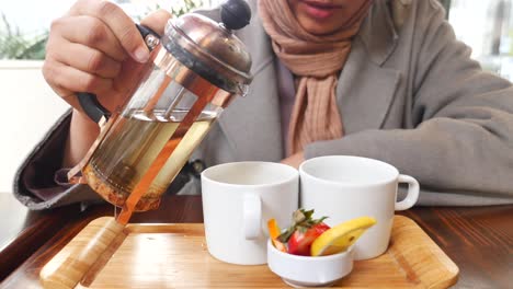 woman pouring tea from a french press into a white cup