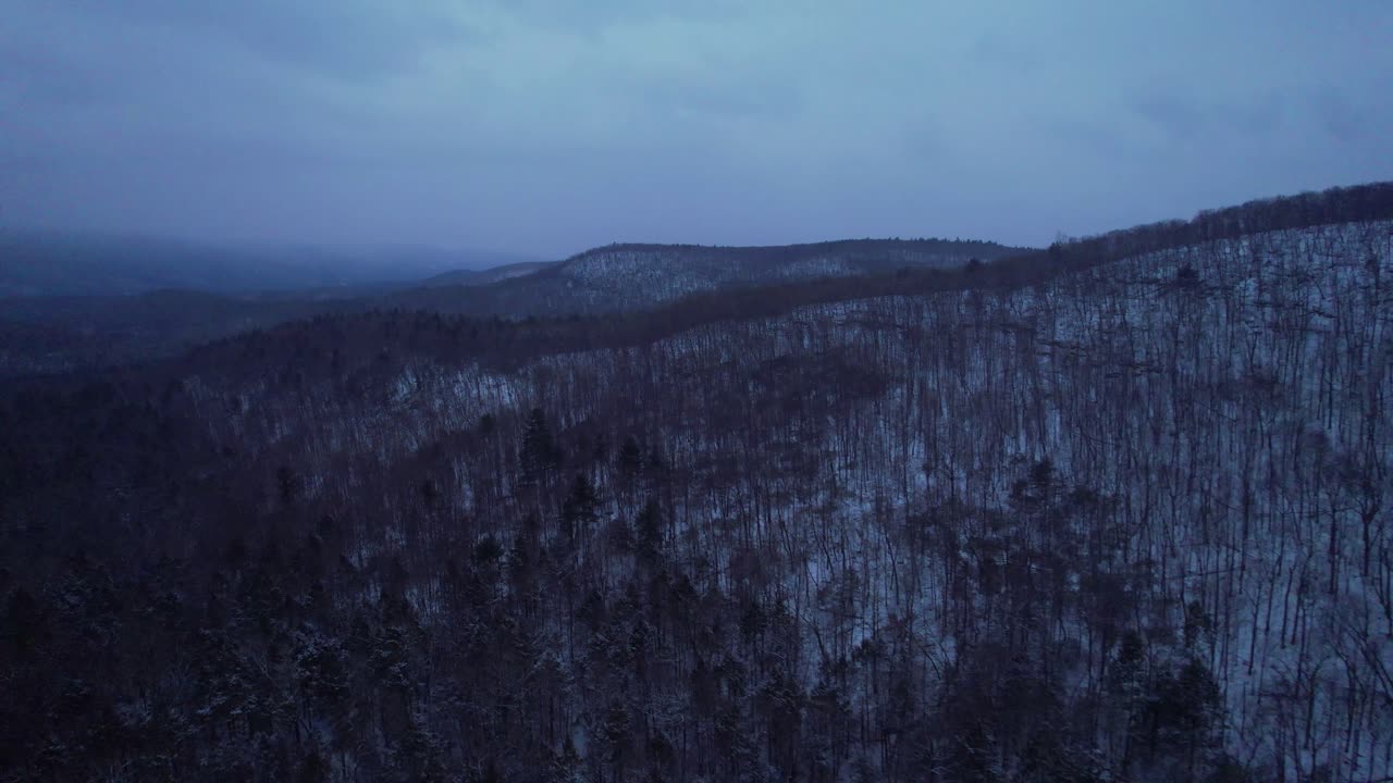 Aerial drone video footage of nightfall in the snowy Appalachian mountains during winter, in the Catskill Mountains sub-range