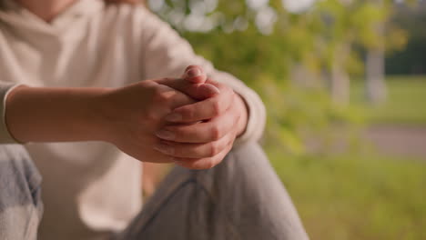 individual with hands clasped together, conveying calm and introspection against a softly blurred green background, with leaves swaying in the breeze in background