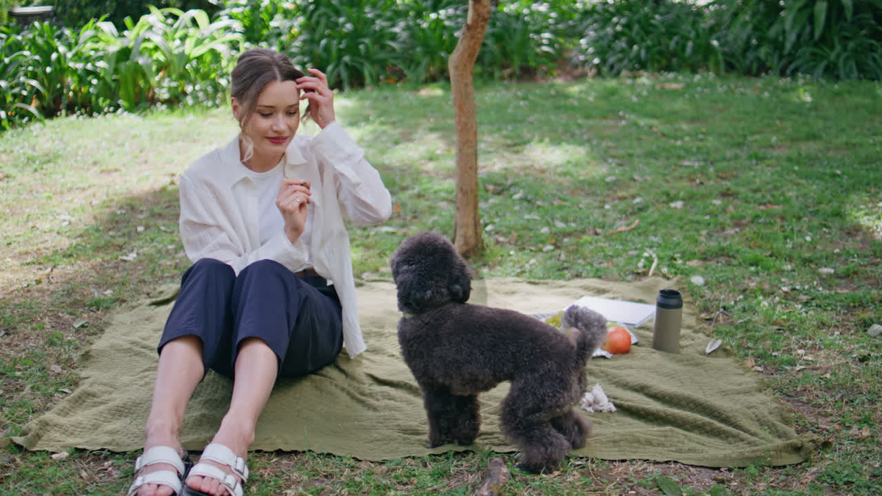 Woman enjoying picnic dog in green park. Relaxed girl bonding with black poodle