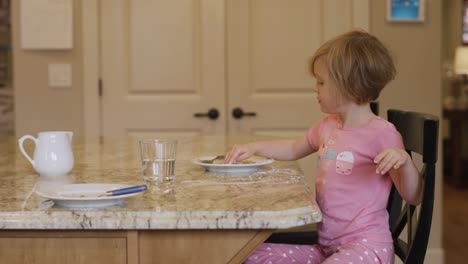 una niña pequeña comiendo azúcar en polvo de su plato con sus dedos, con su perro mendigando cerca