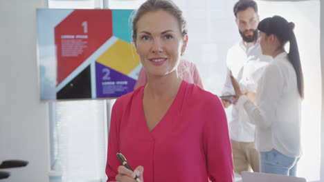 Portrait-of-happy-caucasian-businesswoman-over-diverse-colleagues-in-office