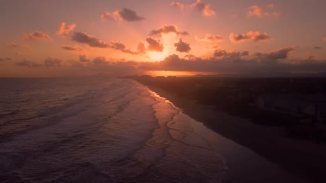 Tilting-aerial-shot-of-beach-in-sunset,-beautiful-sky-and-waves