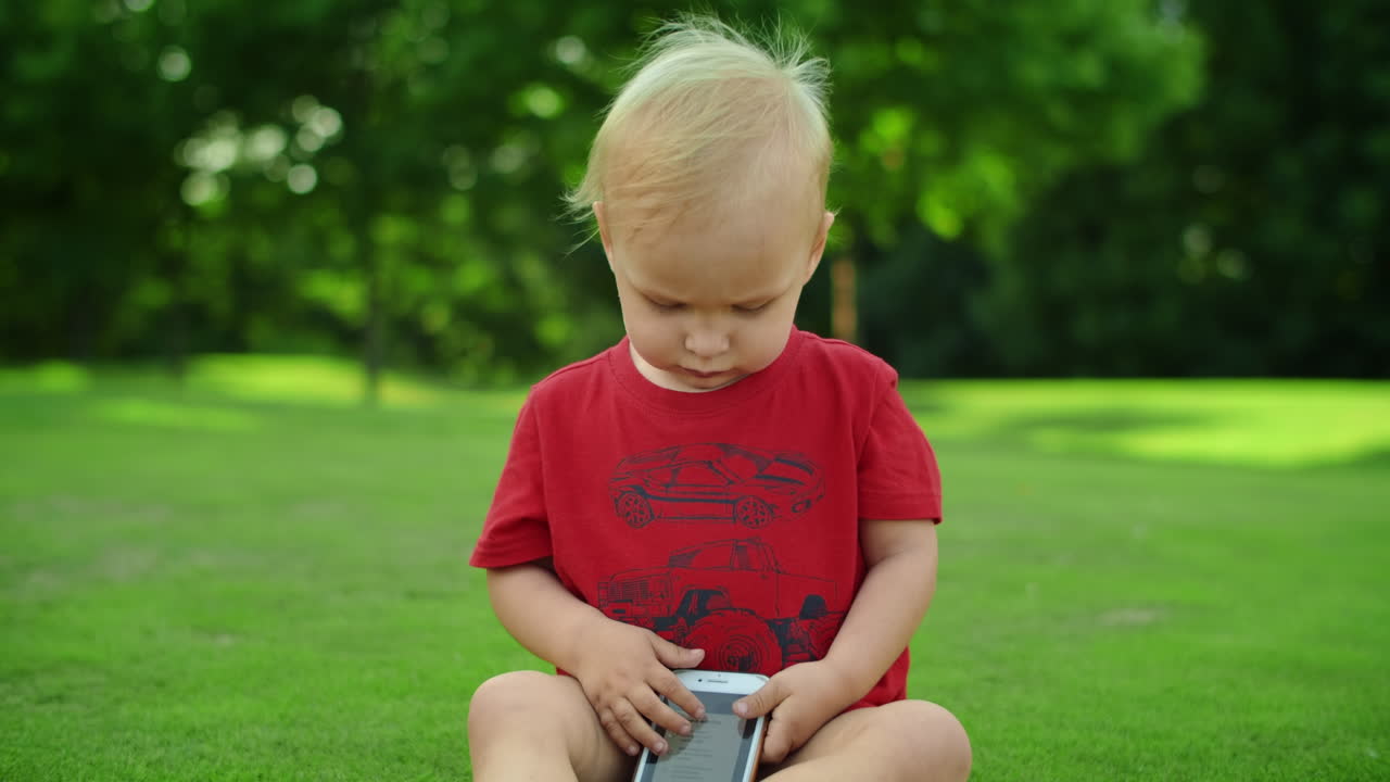 Kleinkind sitzt auf grüner Wiese mit Handy. Süßes Kind hält Handy.